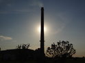 Průmyslová romantika klesajícího Slunce za továrním komínem.
